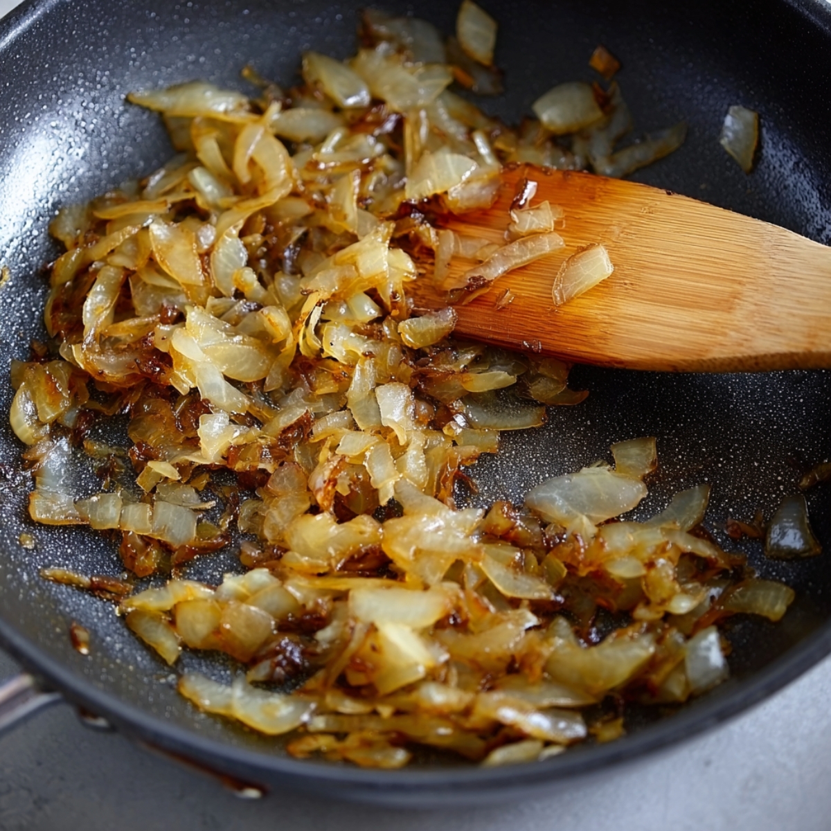 Caramelized onions in a pan, cooked to a rich golden-brown color, with a wooden spoon.