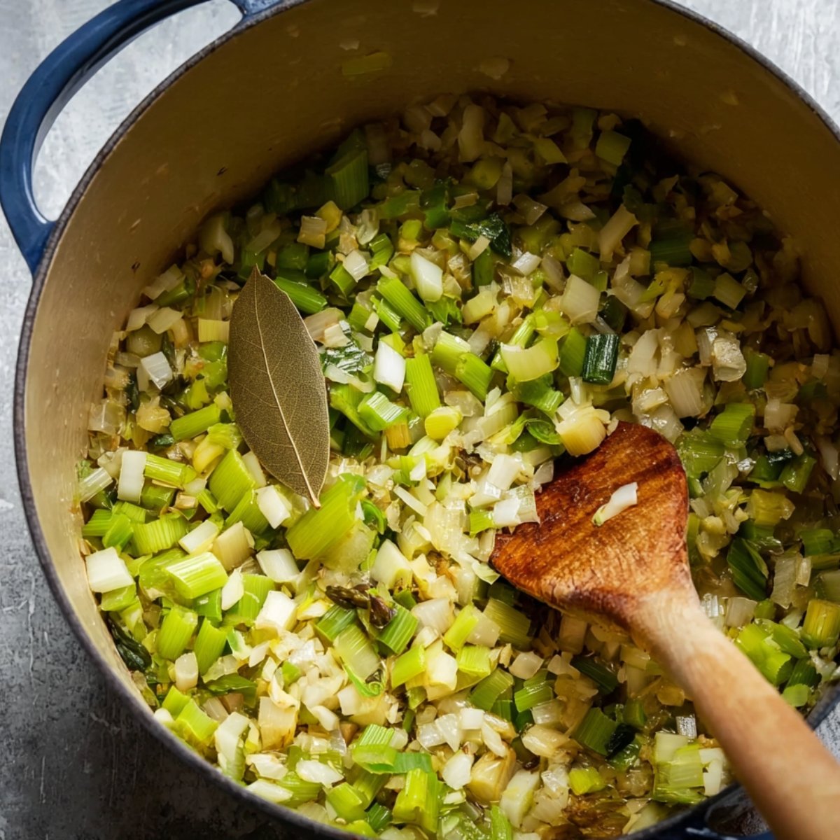 Chopped leeks and onions cooking in a pot with a bay leaf, softened and ready for the next step in making asparagus soup.