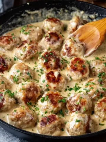 Chicken Meatballs in Cream Sauce in a pan with a wooden spoon stirring them