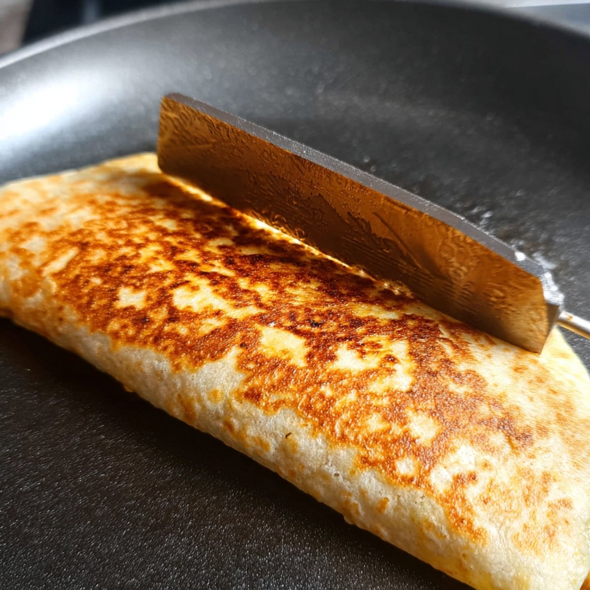 A tuna melt wrap being grilled in a skillet, with a spatula pressing down to create a golden-brown, crispy exterior.