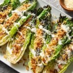 Grilled Romaine Caesar Salad lettuce topped with toasted panko breadcrumbs, grated parmesan, and Caesar dressing, offering a smoky and crunchy twist on the classic Caesar salad.