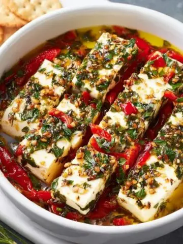 A dish of Marinated Cheese, including slices of cheese and red peppers soaked in an aromatic herb oil marinade.