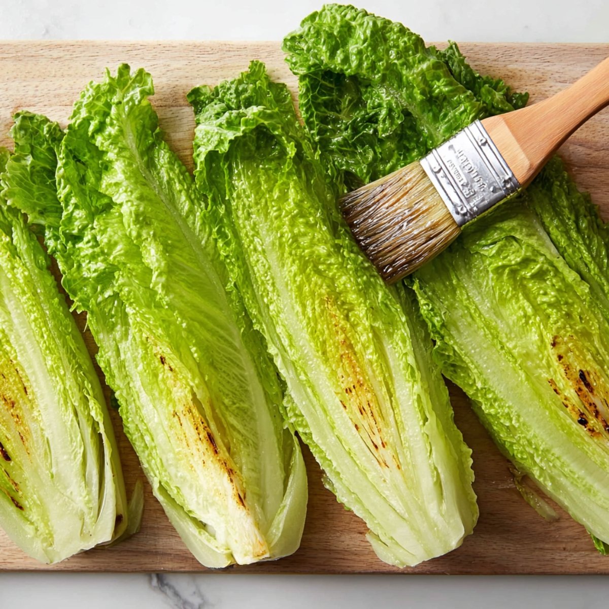 Brushing halved romaine lettuce with oil, preparing it for grilling to enhance its flavor and texture.