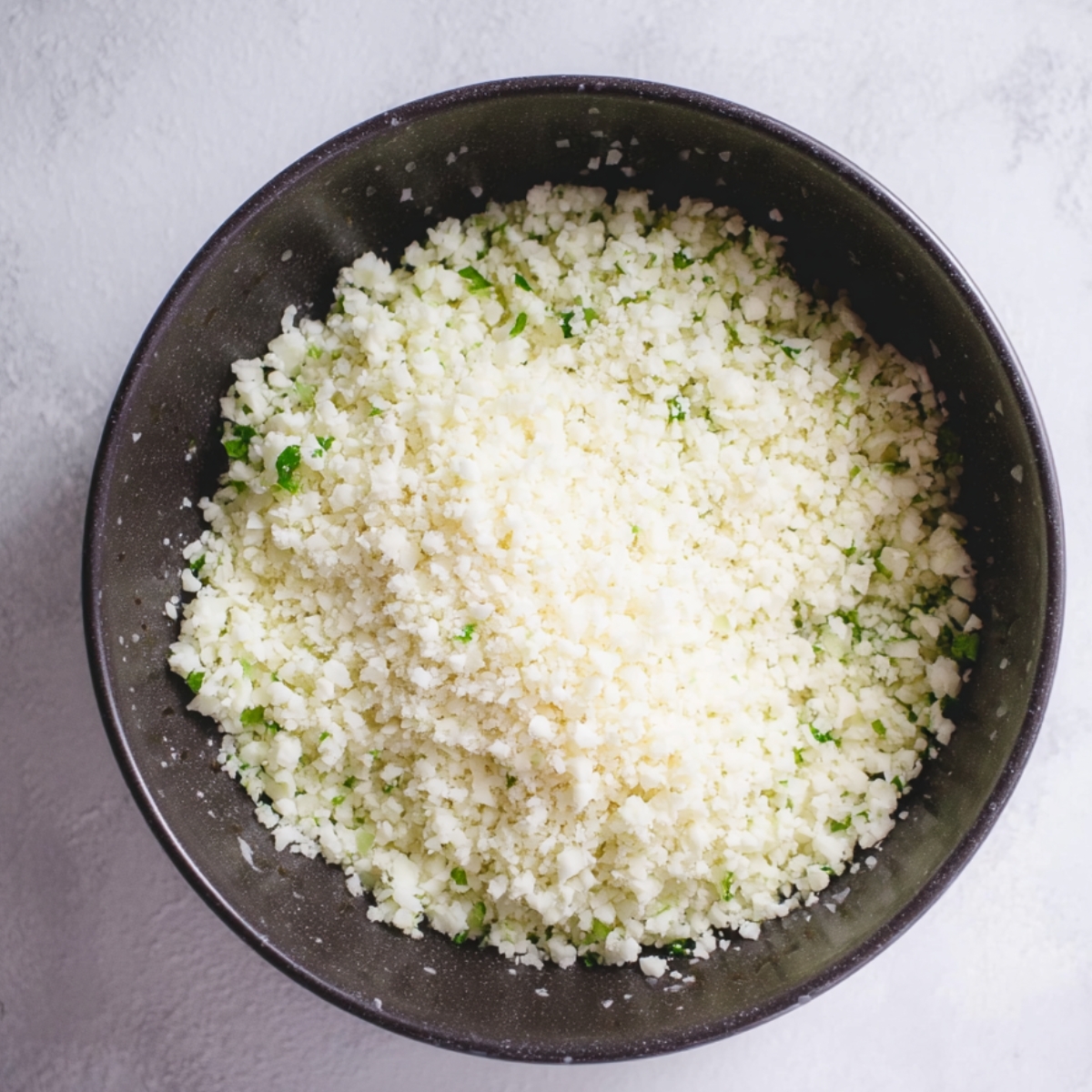 Breaking down cauliflower into florets and green onions in a food processor to create cauliflower rice for a healthy Tabbouleh base.