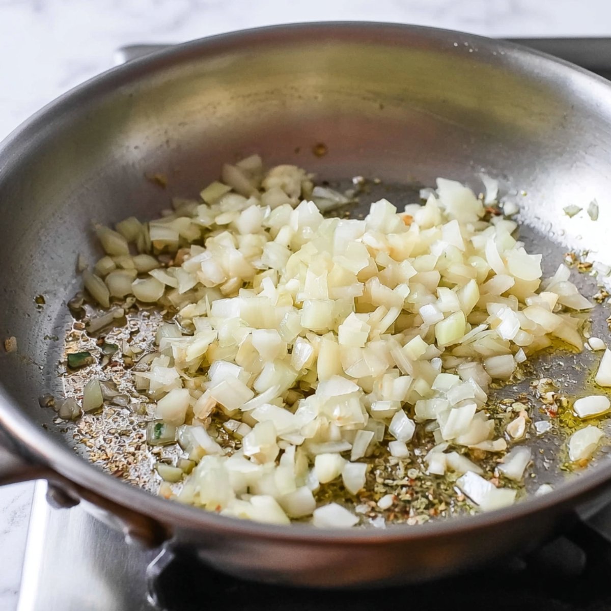 A close-up of diced onions sautéing in a skillet with spices, creating a fragrant base for a savory dish. The onions are softening in oil, and the aroma fills the air.