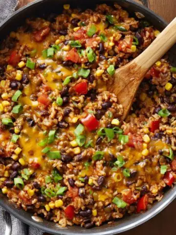 A hearty Southwest Lentils and Rice Skillet with melted cheese, black beans, corn, and diced tomatoes, topped with fresh green onions for garnish.