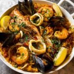 A vibrant Spanish Paella with shrimp, squid, and mussels garnished with parsley and lemon wedges, showcasing Spanish flavors.