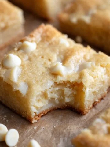 A deliciously baked White Chocolate Brownies with a bite taken out, revealing its soft, gooey texture and scattered white chocolate chips.