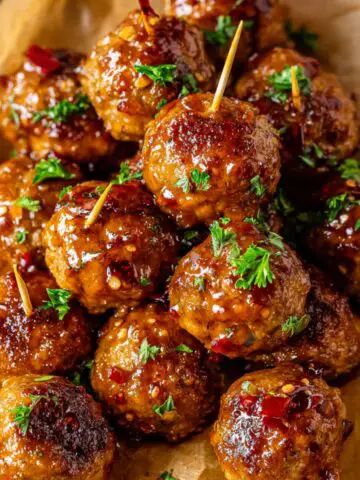 A close-up of glossy glazed Air Fryer Firecracker Chicken Meatballs garnished with parsley, topped with toothpicks, and a hint of chili flakes for extra flavor.