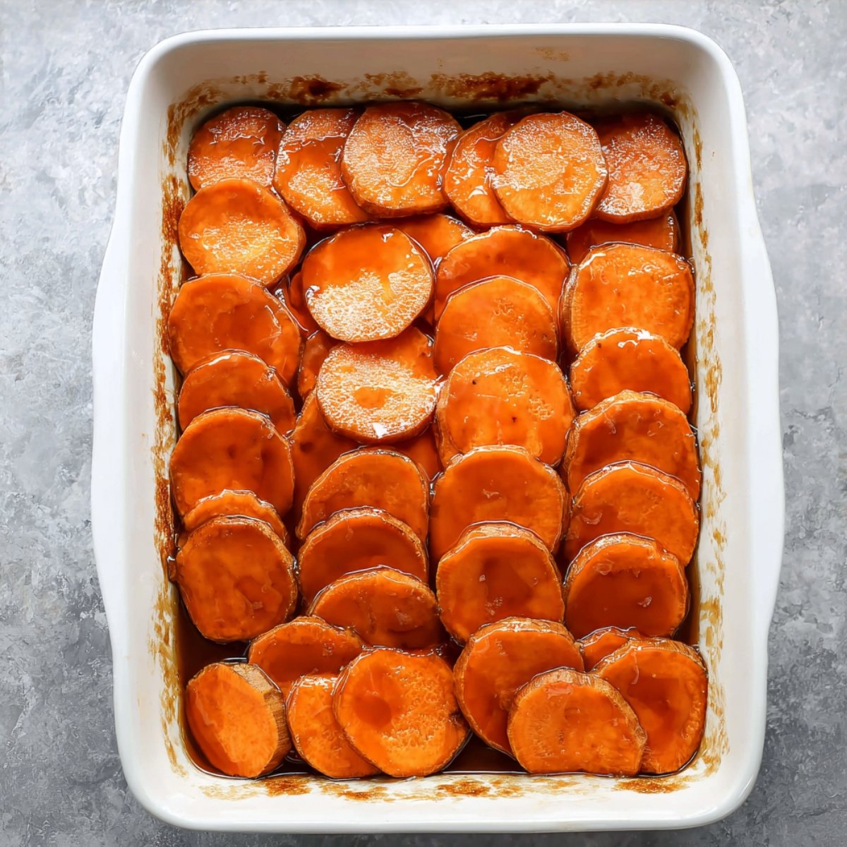 Layered sweet potatoes in a baking dish, covered with syrup before baking.