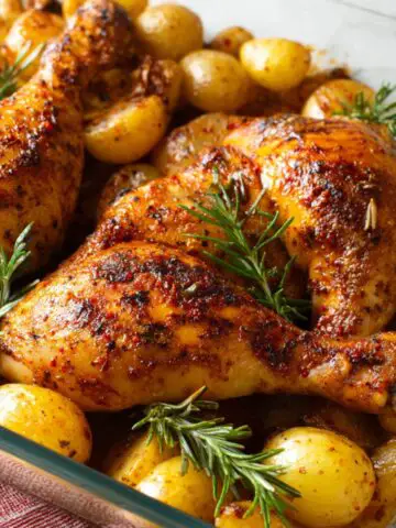 Baked Chicken Leg Quarters surrounded by roasted baby potatoes and fresh rosemary sprigs, showing a deliciously seasoned dish.