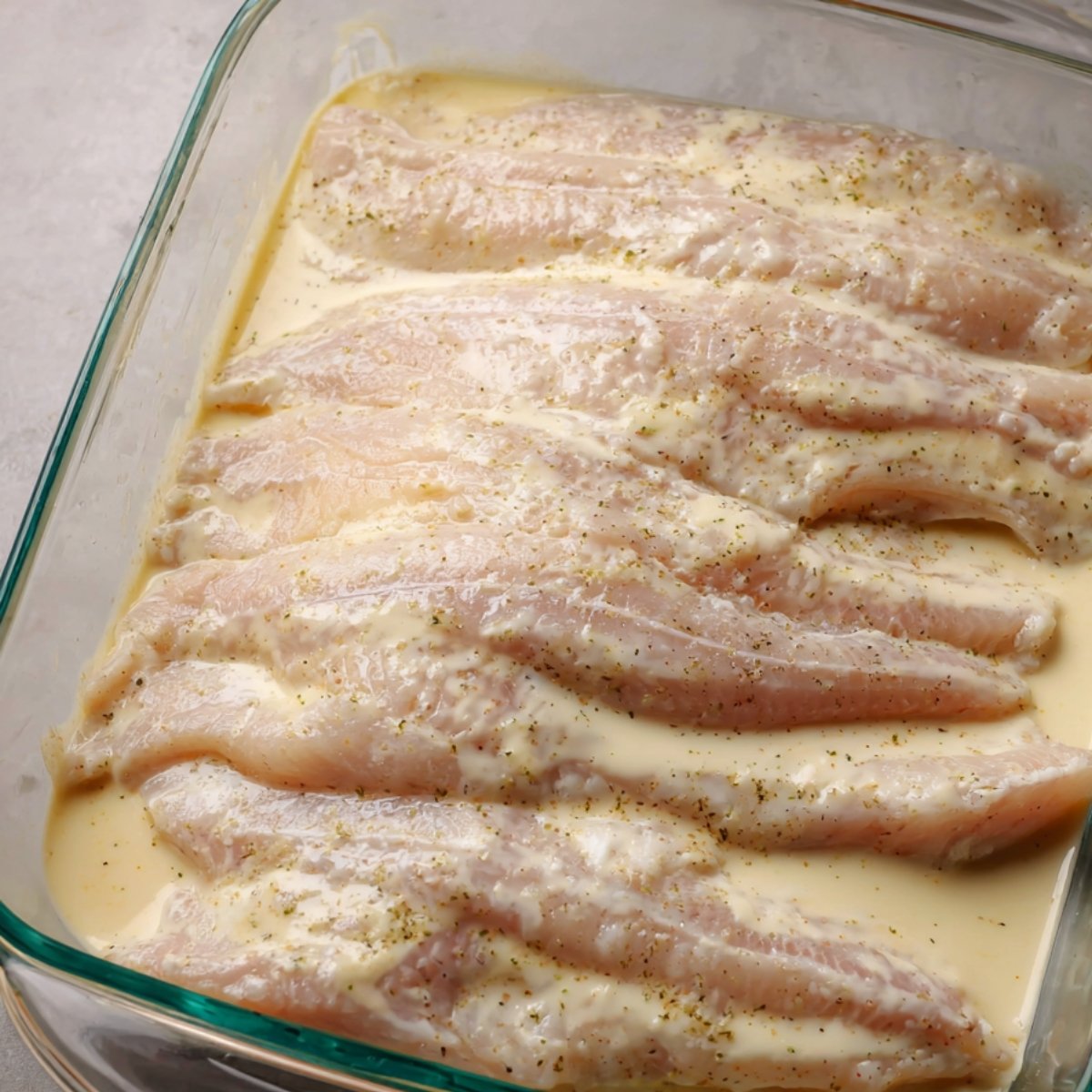 Catfish fillets soaking in a milk and seasoning brine mixture, preparing them for cooking.