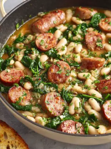 A hearty Chicken Sausage White Bean Skillet, with fresh spinach, beans, and sausage slices cooked together in a savory broth, garnished with parsley.