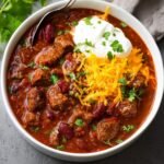 A hearty bowl of Chili Con Carne topped with shredded cheese, sour cream, and fresh cilantro.