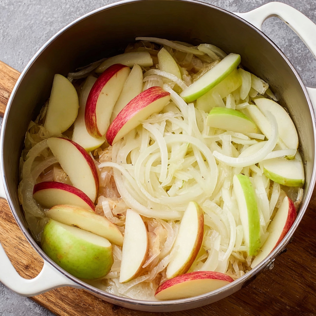 Cooking onions and apples for Pork and Sauerkraut: Thinly sliced onions and apples in a Dutch oven, simmering together, adding flavor to a savory dish.