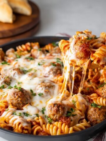 A skillet filled with a delicious Dump and Bake Meatball Casserole, topped with melted cheese and garnished with parsley, ready to be served with crusty bread.