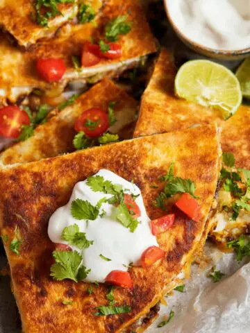 Sheet Pan Crunchwrap with toppings of sour cream, tomatoes, and cilantro placed on top, along with lime wedges.