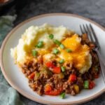 A delicious serving of Sloppy Joe Casserole with seasoned ground beef, topped with melted cheese and served alongside creamy mashed potatoes, garnished with fresh green onions.